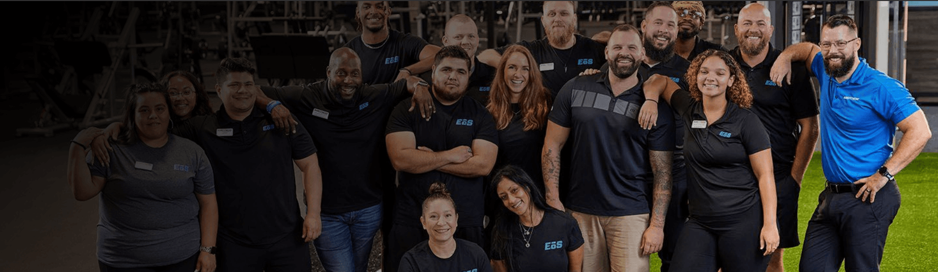 group shot of many eos staff members shoulder to shoulder smiling inside of a eos branded box gym