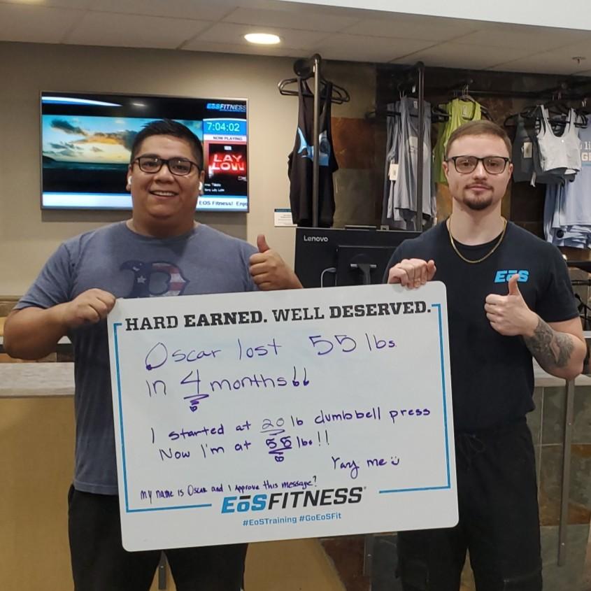 eos gym member standing side by side with personal trainer holding a white board listing oscar lost weight  and gaining strength from personal training