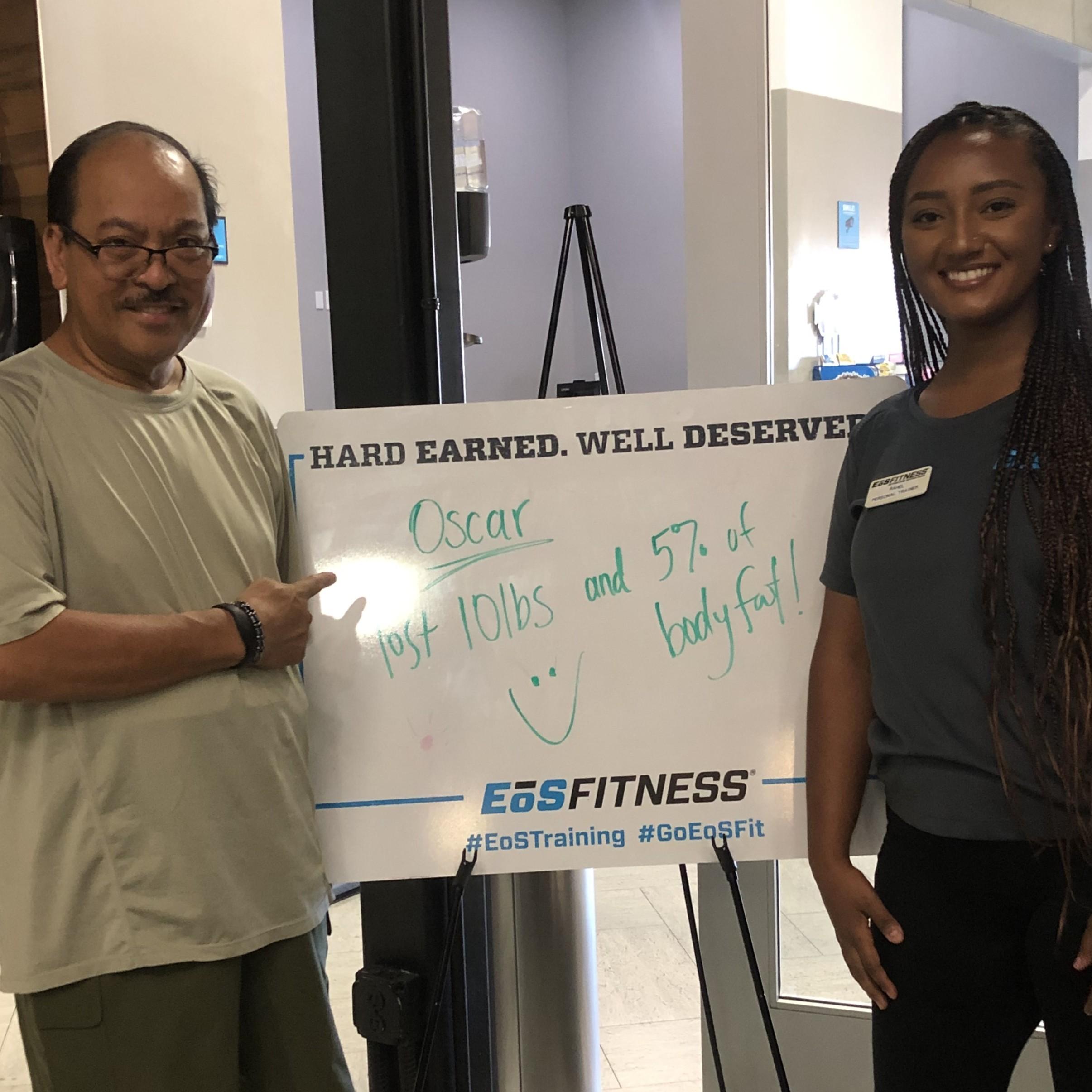 eos gym member standing side by side with personal trainer holding a white board listing oscar lost weight from personal training