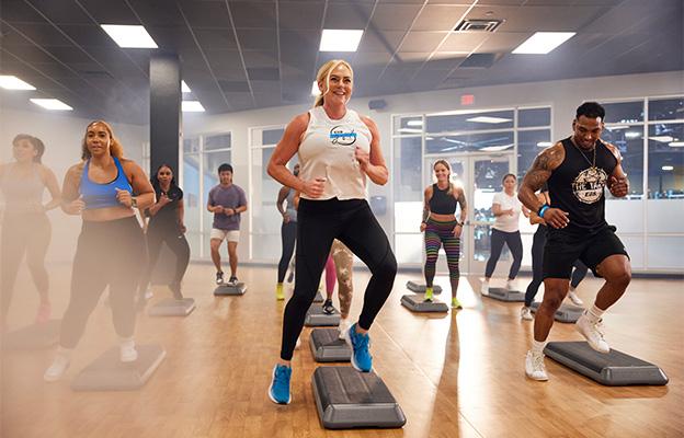 a group of eos gym members in a step class inside a well lit studio