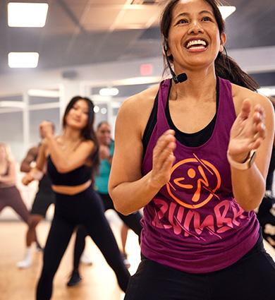 smiling zumba instructor leading a group of eos gym members in a well lit studio