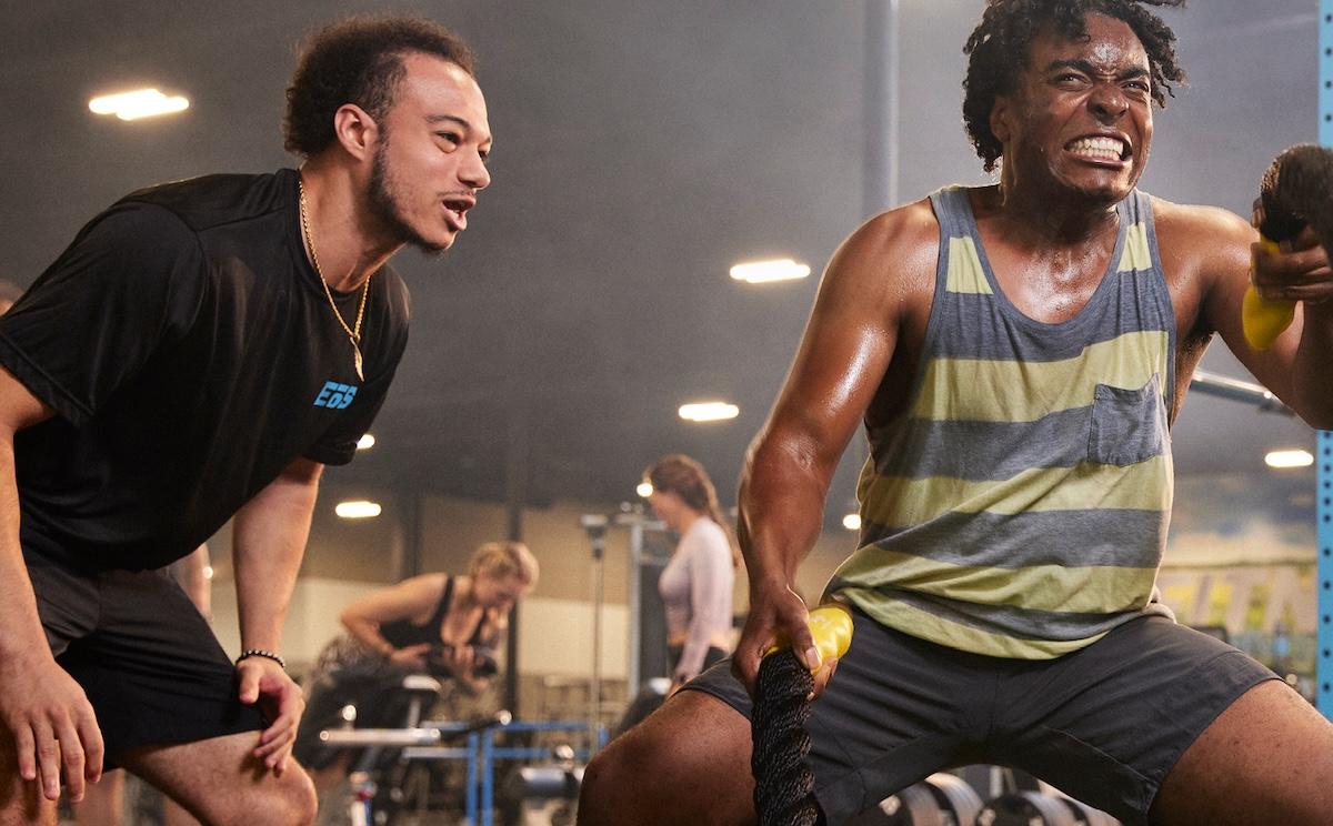 Crop image of beautiful sport girl with dumbbell in hand with personal trainer in professional gym