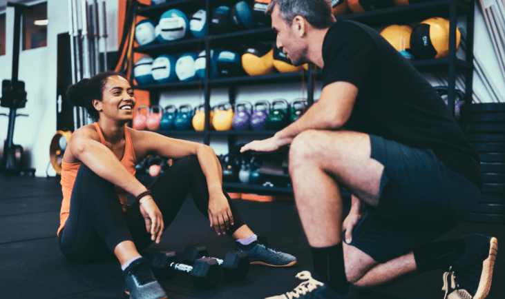 personal trainer kneeling down and helping eos gym member