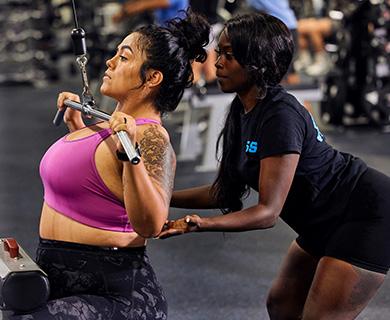 Personal trainer assisting a woman with a lat pulldown exercise in the gym