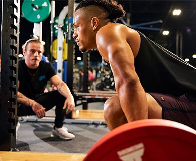Trainer observing and motivating a man performing a heavy lift in the gym