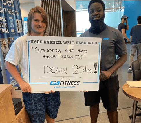 eos gym member standing side by side with personal trainer holding a white board listing how much weight they lost