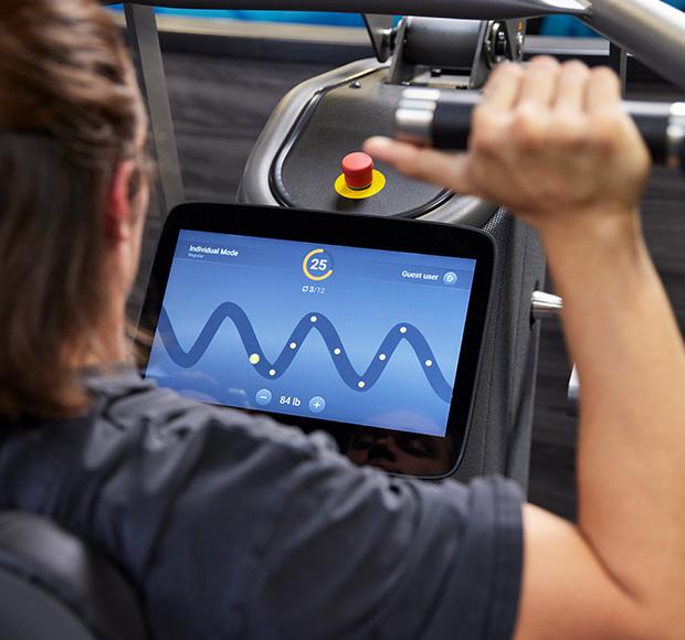 eos gym member shoulder pressing on a piece of smart equipment