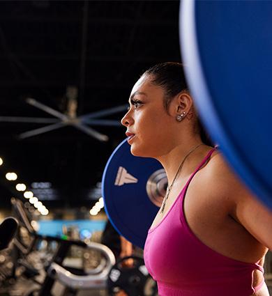 Focused woman lifting a barbell with blue weight plates at the gym