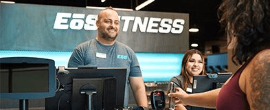 two smiling staff members helping an eos gym goer check in