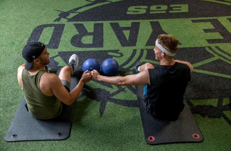 two eos gym members sitting on yoga mats inside a eos branded gym fist bumping