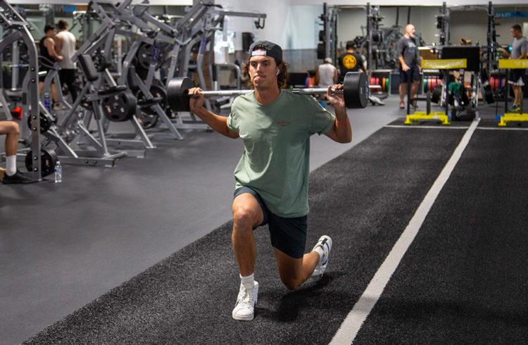 eos gym member doing barbell lunges on turf