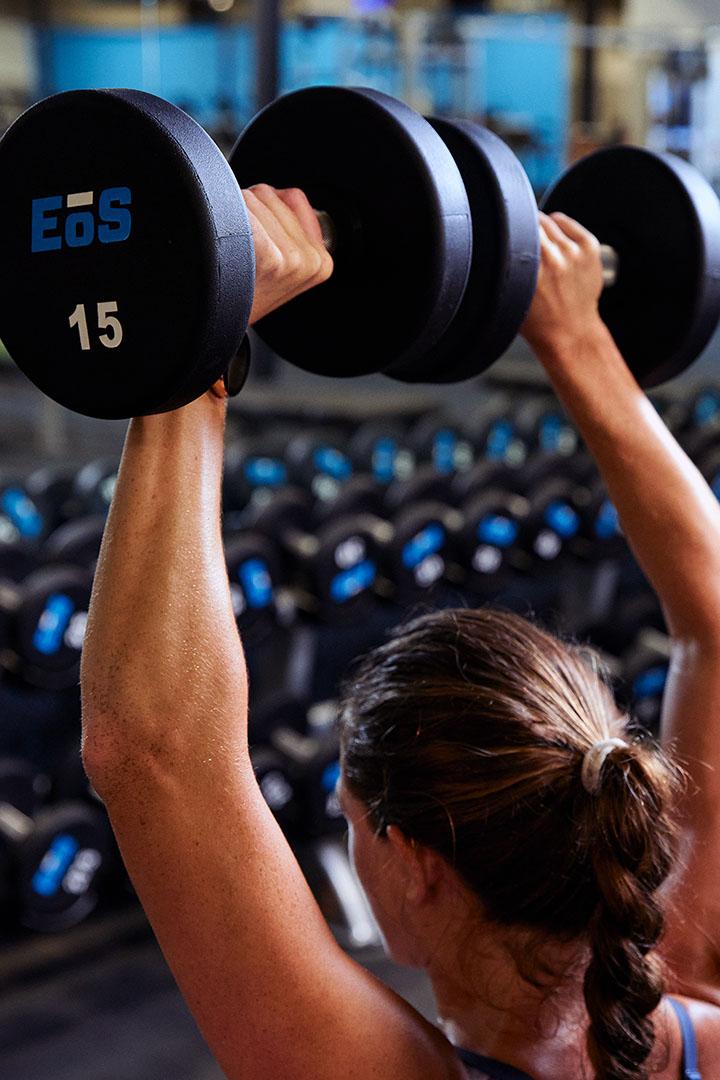 eos member lifting two 15lbs dumbbells over their head