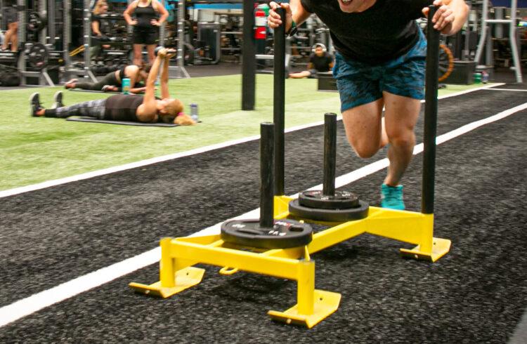 eos gym member pushing a sled on eos branded indoor turff