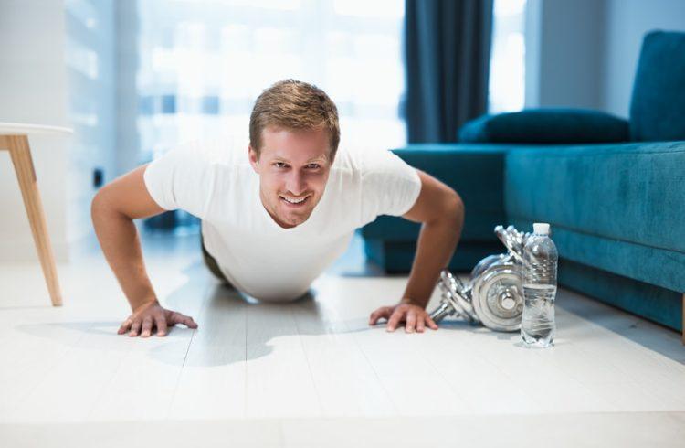 Man doing push-ups at home next to dumbbells and a water bottle
