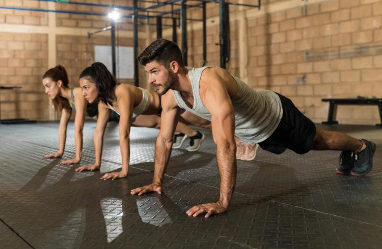 Confident young male and female athletes doing push-ups during cross training at gym