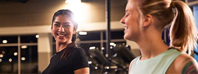 two eos gym members smiling at each other is a brightly lit gym