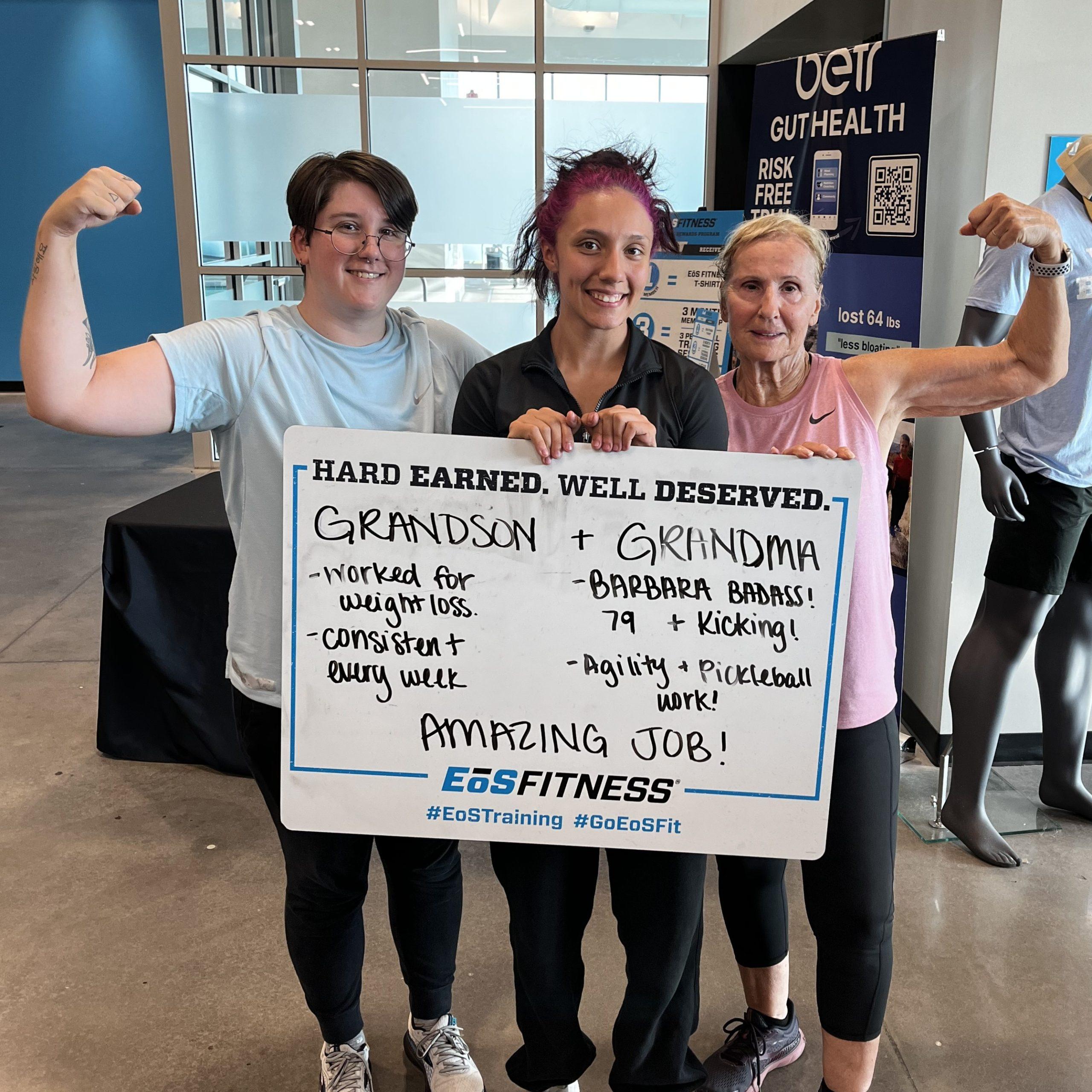 eos gym members standing side by side with personal trainer holding a white board listing family getting stronger and lost weight from personal training