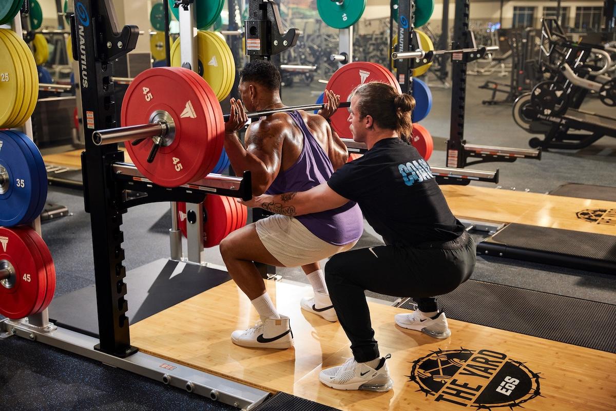 eos gym member doing squats with trainer spotting