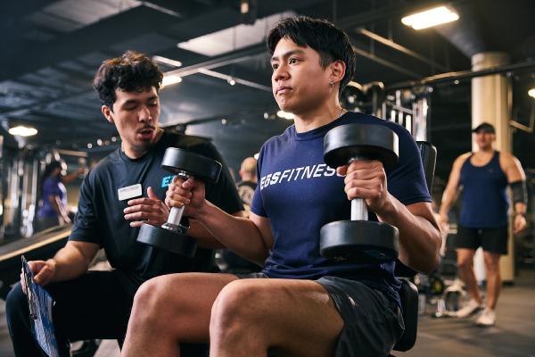 eos gym member getting help from pt on dumbell press