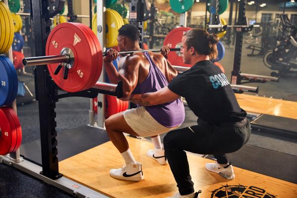 eos gym member getting help from pt on barbell squat