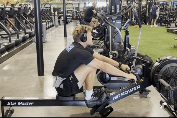 EōS Fitness member performing EZ-bar curls in the gym.